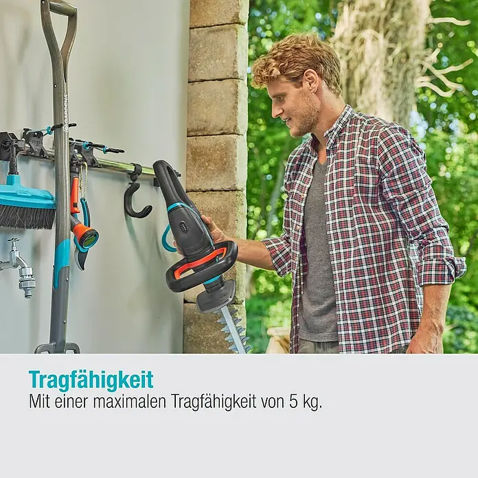 Gardena Halterung Set Einzelhalter & Einzelhaken - Traglast: 10 kg, Aluminium - Ein Mann betrachtet eine Gardena Akku-Grasschere mit ihren scharfen Klingen, die an einer Werkzeugaufhängung befestigt ist.
