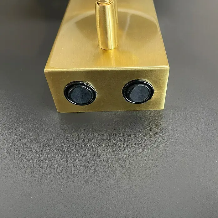 Fischer & Honsel Wandleuchte Dreamer - 44 W, L x B x H: 26 x 16 x 28 cm, Messing, Weiß, E27, 2 Stk., Mit Lesearm - Nahaufnahme einer goldenen Lampe mit zwei runden, schwarzen Schaltern, die auf einer grauen Oberfläche steht. Die Lampe ist minimalistisch gestaltet.