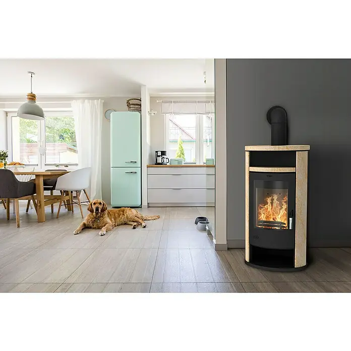 Fireplace Kaminofen Alicante Loticstone - 8,3 kW, Raumheizvermögen: 126 m³, Material Verkleidung: Speckstein, Schwarz - Gemütliches Wohnzimmer mit einem Kaminofen mit Steinverkleidung, der Wärme und Stil in den Raum bringt. Ein Golden Retriever liegt entspannt auf dem Boden.