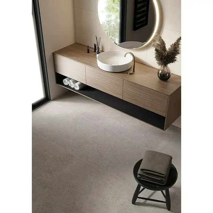 Feinsteinzeugfliese Big Sand - 60 x 60 cm, Beige, Matt - Ein elegantes Badezimmer mit einem Waschtisch aus hellem Holz, einem runden Waschbecken und einem beleuchteten Spiegel. Graue Fliesen vervollständigen den Look.