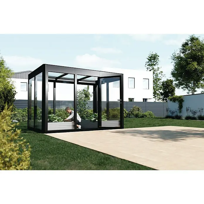 SunElements Gewächshaus SunGarden Infinity 3.2 - Außenmaß inkl. Dachüberstand (B x T): 338 x 233 cm, Material Seitenwand: Kunststoff, 6 mm, Anthrazit-Metallic - Ein modernes Gewächshaus mit schwarzem Rahmen und Glaswänden, in dem eine Person gärtnert. Das Gewächshaus steht auf einer Holzterrasse.