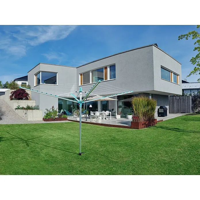 Leifheit Wäschespinne Linomatic 500 Easy Wäscheschirm - Geeignet für Anzahl Waschmaschinenfüllungen: 5 Stk., Länge Wäscheleine: 50 m, Durchmesser offen: 3,28 m, Grau/Metallic, Mint - Wäschespinne im Garten vor einem modernen Haus. Die Wäschespinne ist mit Leinen zum Trocknen von Kleidung ausgestattet und steht auf einem grünen Rasen.