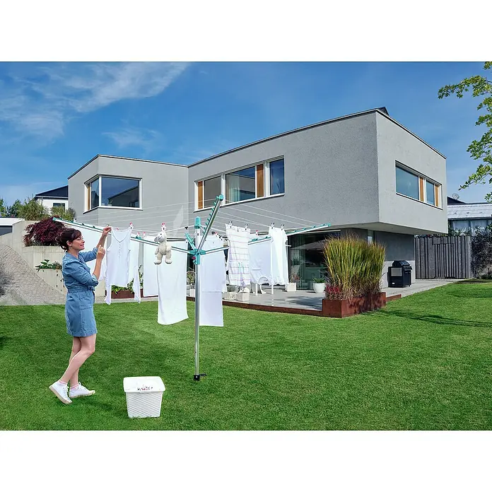 Leifheit Wäschespinne Linomatic 500 Easy Wäscheschirm - Geeignet für Anzahl Waschmaschinenfüllungen: 5 Stk., Länge Wäscheleine: 50 m, Durchmesser offen: 3,28 m, Grau/Metallic, Mint - Eine Frau hängt Wäsche auf einer drehbaren Wäschespinne im Garten auf. Die Leifheit Wäschespinne bietet viel Platz zum Trocknen im Freien.