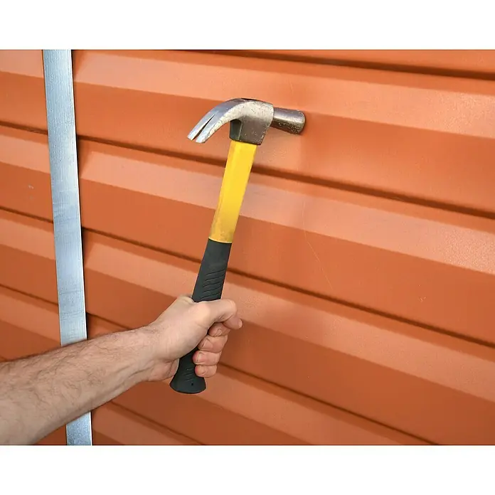 Palram – Canopia Caseta de jardín Skylight - Medidas ext. (An x Pr): 121 x 176 cm, Plástico, Ámbar - Primer plano de un martillo con mango amarillo clavado en una superficie naranja corrugada, junto a una tira de metal.