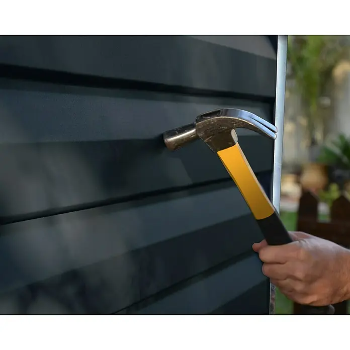 Palram – Canopia Caseta de jardín Skylight - Medidas ext. (An x Pr): 185 x 229 cm, Plástico, Antracita - Un martillo con mango amarillo clava un clavo en una superficie de madera azul oscuro. La herramienta se utiliza para reparar o construir.