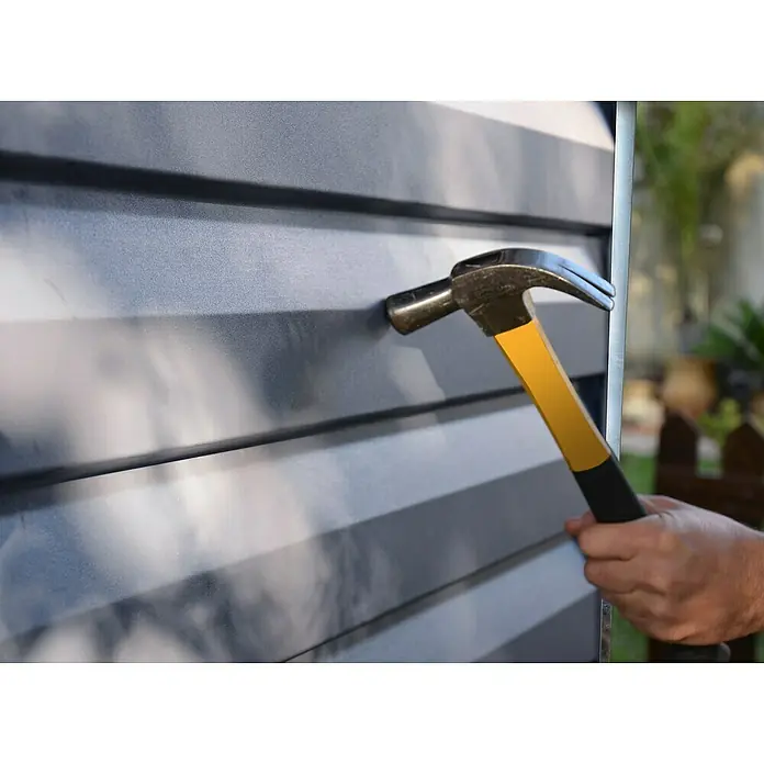 Palram – Canopia Caseta de jardín Skylight - Medidas ext. (An x Pr): 185 x 229 cm, Plástico, Antracita/gris - Un martillo con mango amarillo clava un clavo en una pared gris, presumiblemente para asegurar algo. Herramienta en acción.