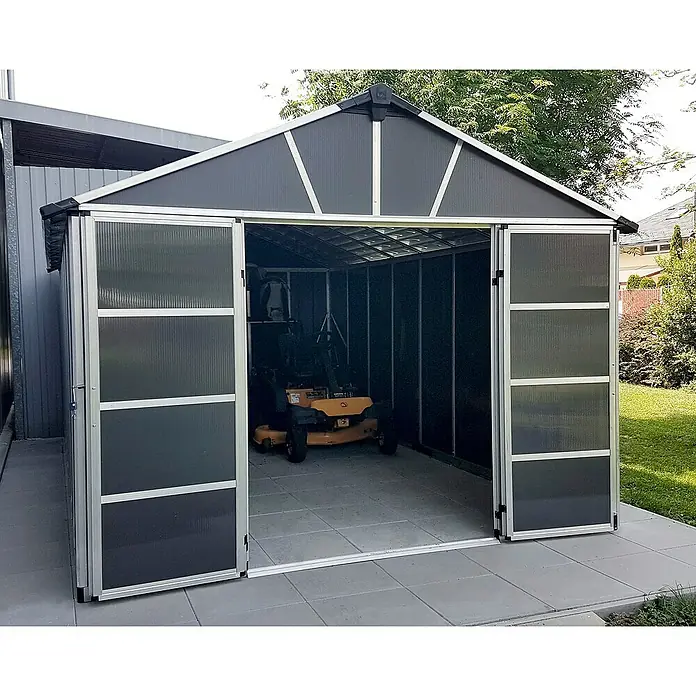 Palram – Canopia Caseta de jardín Yukon - Medidas ext. (An x Pr): 332 x 643 cm, Plástico, Antracita/Plata, Sin suelo - Un espacioso cobertizo de jardín gris con puertas dobles se sitúa sobre un área pavimentada, proporcionando almacenamiento para herramientas.