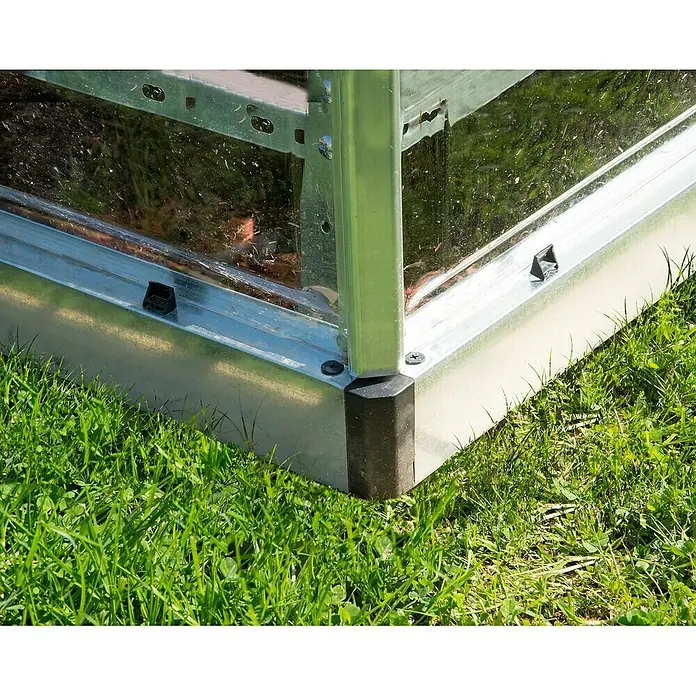 Palram – Canopia Invernadero Lean To - Medidas ext. (An x Pr): 123,8 x 243,8 cm, Material de la pared lateral: Plástico, 0,7 mm, Plateado - Primer plano de una base de invernadero de metal con una esquina negra, rodeada de hierba verde.