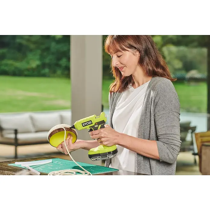 Ryobi ONE+ Akku-Heißklebepistole RGLU18-0 - 18 V, Ohne Akku, Durchmesser Klebepatrone: 11 mm - 12 mm - Frau verwendet eine Ryobi-Heißklebepistole, um ein Seil an einem gelben Bastelprojekt zu befestigen.