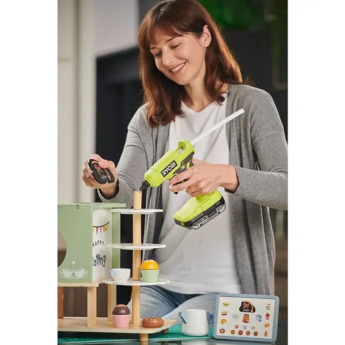 Ryobi ONE+ Akku-Heißklebepistole RGLU18-0 - 18 V, Ohne Akku, Durchmesser Klebepatrone: 11 mm - 12 mm - Frau benutzt eine RYOBI Klebepistole zum Basteln an einem Spielzeugcafé.