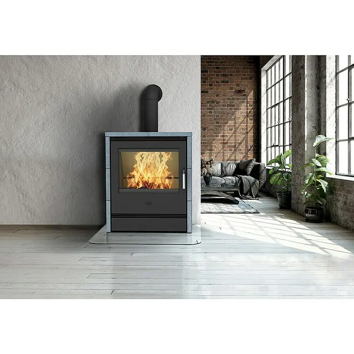 Fireplace Kaminofen Rönky - 9 kW, Raumheizvermögen: 180 m³, Material Verkleidung: Speckstein, Schwarz - Ein moderner Kaminofen mit brennendem Feuer in einem stilvollen Wohnraum. Der Kamin steht auf einem Glasuntergrund vor einer grauen Wand.