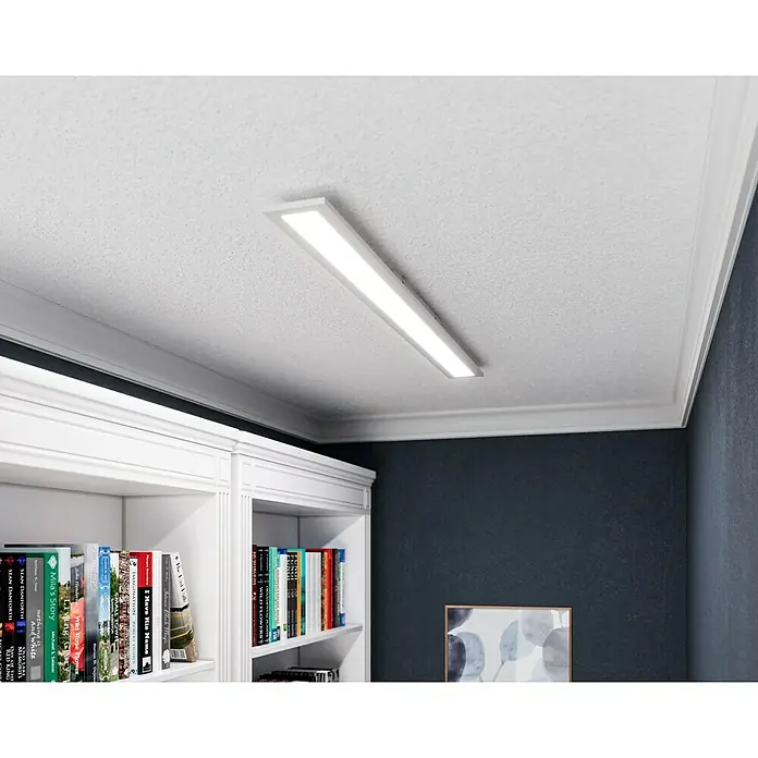 Tween Light LED-Panel RC-CCT-DIM - 22 W, L x B x H: 120 x 10 x 5 cm, Weiß, Mehrfarbig - Eine schlanke Deckenleuchte ist an einer weißen Decke montiert und beleuchtet ein Bücherregal und eine Wand.