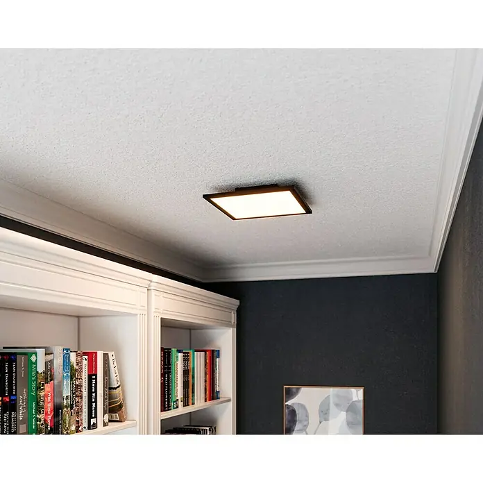 Tween Light LED-Panel CCT-RC-DIM - 15,5 W, L x B x H: 29,5 x 29,5 x 5 cm - Eine moderne, quadratische Deckenleuchte mit einem schlanken, dunklen Rahmen erhellt einen Raum mit Bücherregal und Akzentwand.