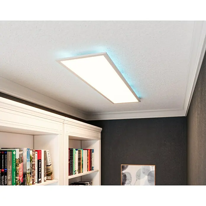 Tween Light LED-Panel RC-CCT-DIM-RGB-Backlight - 36 W, L x B x H: 120 x 30 x 5 cm, Weiß, RGBW - Eine moderne LED-Deckenleuchte mit blauem Lichtakzent, die in einem stilvollen Raum mit Bücherregal und dunkler Wand montiert ist.