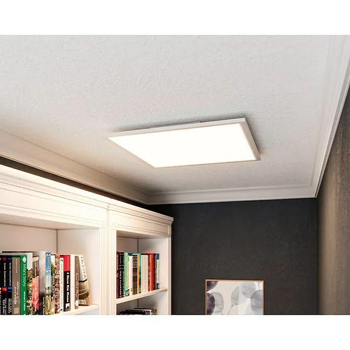 Tween Light LED-Panel RGB-RC-CCT-DIM32,5 W, L x B x H: 59,5 x 59,5 x 5,5 cm, Weiß, RGBW - Die LED-Deckenleuchte erhellt den Raum unter einer Stuckdecke, während sie über einem Bücherregal mit einer dunklen Wand im Hintergrund hängt.