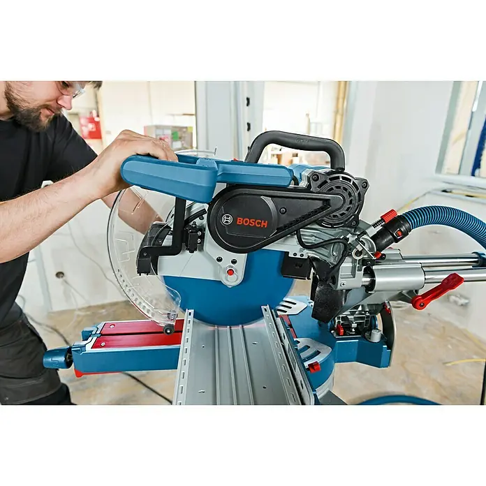 Bosch Professional Paneelsäge GCM 12 SDE - 1.800 W, 3.100 U/min - 4.000 U/min, Durchmesser Sägeblatt: 305 mm, Schnitttiefe: 85 mm bei 90 °/90 ° - Nahaufnahme einer Bosch Kapp- und Gehrungssäge in Aktion mit Bediener, ideal für präzise Holzarbeiten und Heimwerkerprojekte.