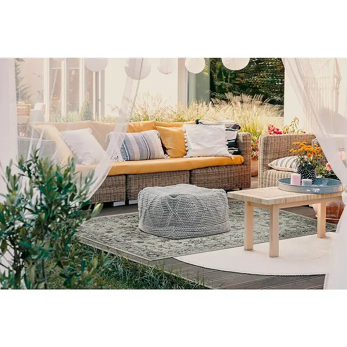 Outdoor-Teppich Austin - Hellgrau, 190 x 133 cm, 100 % Polypropylen - Eine stilvolle Terrasse mit einem bequemen Rattansofa, einem Pouf und einem Beistelltisch, ideal zum Entspannen im Freien.
