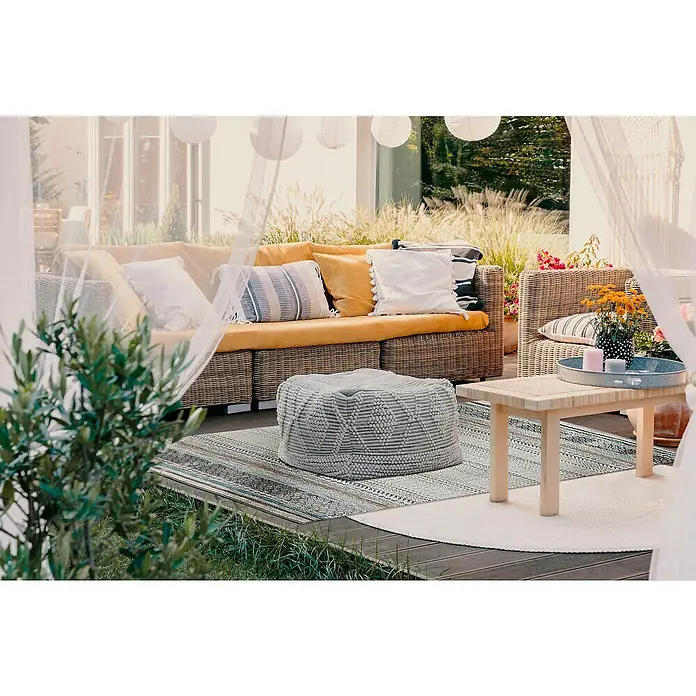 Outdoor-Teppich AustinGraublau, 190 x 133 cm, 100 % Polypropylen - Gemütlicher Außenbereich mit Rattanmöbeln, weichen Kissen und einem grauen Strickpuff auf einem gemusterten Teppich, ideal zum Entspannen.