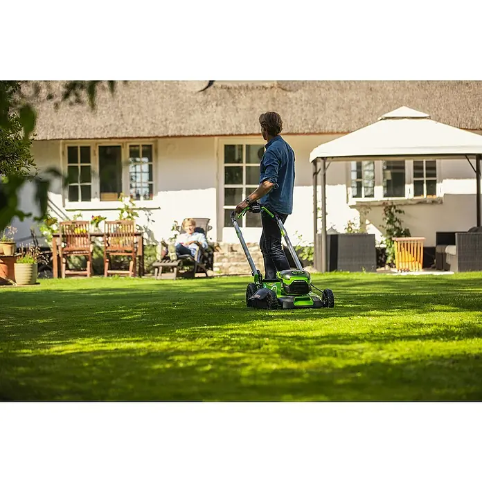Greenworks 60V Akkusystem Akku-Rasenmäher GD60LM46SP - 60 V, Ohne Akku, Schnittbreite: 46 cm - Ein Mann mäht den Rasen mit einem Greenworks-Rasenmäher in einem schönen Garten. Der Rasenmäher ist grün und schwarz.