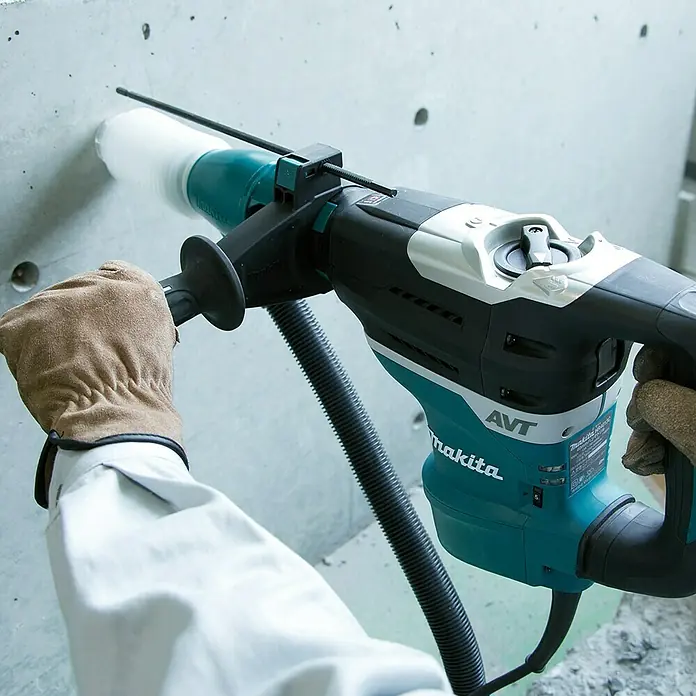 Makita Martillo combinado HR4013C - 1.100 W, 8 J, Alojamiento SDS-MAX - Un martillo rotatorio Makita en acción, perforando un agujero en una pared de hormigón, con extracción de polvo para un trabajo limpio.