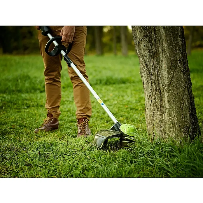 Greenworks 60V Akkusystem Akku-Rasentrimmer GD60LT - 60 V, Li-Ionen, Ohne Akku, Schnittbreite Faden: 40 cm - Mann verwendet einen Rasentrimmer, um Gras um einen Baum herum zu schneiden. Der Rasentrimmer ist grün und schwarz.