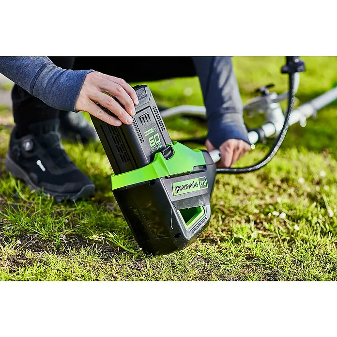 Greenworks 60V Akkusystem Akku-Rasentrimmer GD60BCB - 60 V, Li-Ionen, Ohne Akku, Schnittbreite Messer: 26 cm, Schnittbreite Faden: 40 cm - Nahaufnahme einer Greenworks Pro Akku-Motorsense mit eingesetztem 60-Volt-Akku auf einer grünen Rasenfläche.