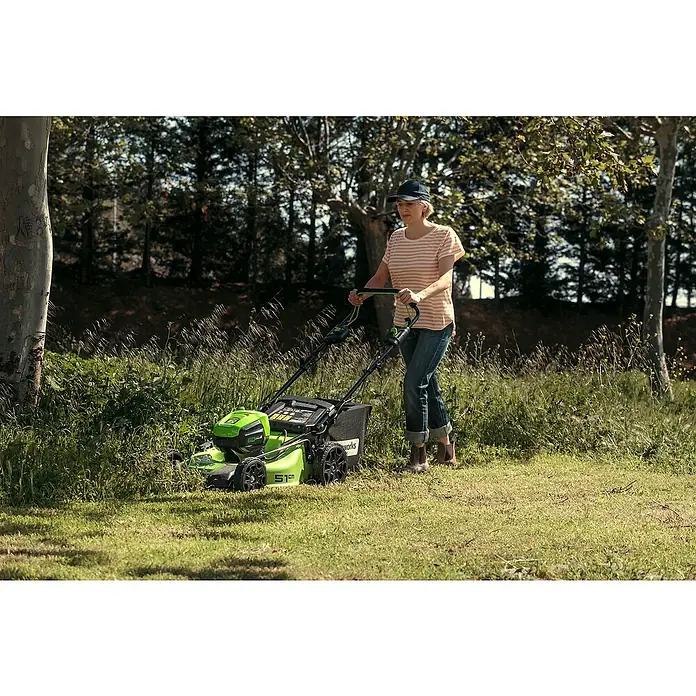Greenworks 60V Akkusystem Akku-Rasenmäher GD60LM51SP - 60 V, 1 Akku, 4 Ah, Schnittbreite: 51 cm - Frau, die einen Greenworks Rasenmäher im Garten benutzt. Kabelloser, grüner Rasenmäher für einen gepflegten Garten.