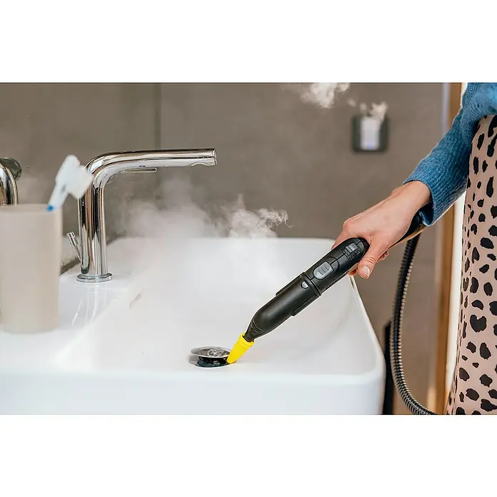 Kärcher Dampfreiniger SC 5 EasyFix Iron Plug - 2.250 W, Aufheizzeit: 3 min, Behältervolumen: 1,5 l - Eine Person reinigt ein Waschbecken mit einem Dampfreiniger. Der schwarze Dampfreiniger hat eine gelbe Düse. Wasserdampf steigt auf.
