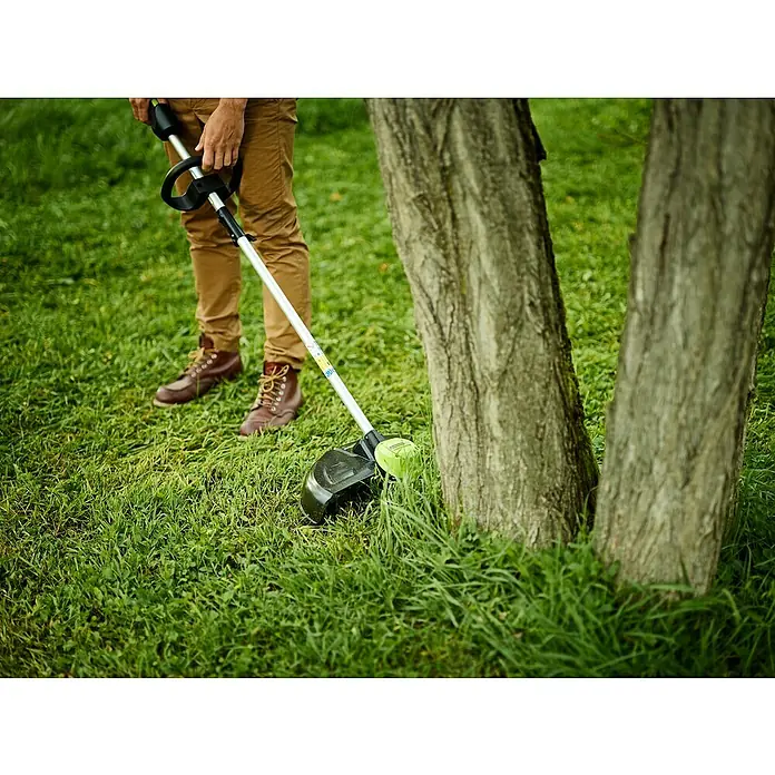 Greenworks 60V Akkusystem Akku-Rasentrimmer GD60LT - 60 V, Li-Ionen, Ohne Akku, Schnittbreite Faden: 40 cm - Rasentrimmer im Einsatz: Eine Person trimmt Gras um Baumstämme herum, für einen gepflegten Garten.