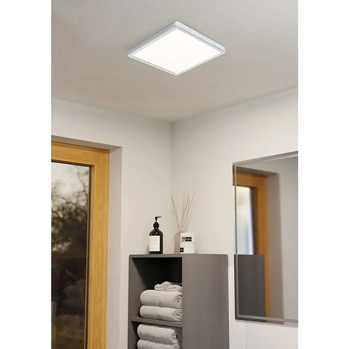 Eglo Fueva 5 LED-Deckenleuchte IP44 - 20 W, L x B x H: 28,5 x 28,5 x 2,8 cm, Chrom, Warmweiß - Eine quadratische Deckenleuchte mit silbernem Rand beleuchtet einen Badezimmerraum mit Handtüchern, Seife und Dekorationen.