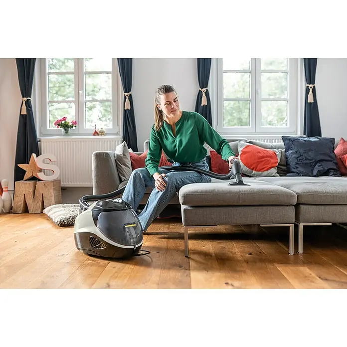 Kärcher Dampfsauger SV 7 - 2.200 W - Eine Frau reinigt mit einem Kärcher-Dampfsauger ein graues Sofa in einem hellen Wohnzimmer. Das Gerät steht auf dem Holzboden bereit.