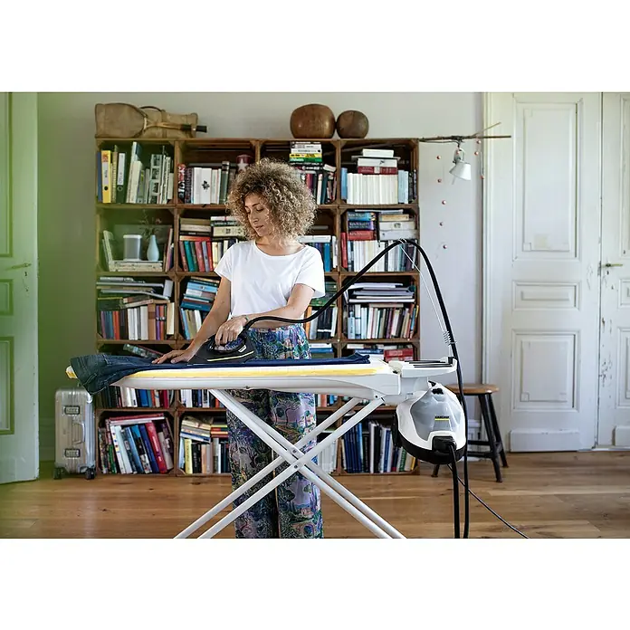 Kärcher Dampfreiniger SC 4 EasyFix Iron - 2.000 W, Aufheizzeit: 4 min, Behältervolumen: 0,8 l - Frau bügelt Wäsche mit einem Kärcher Dampfbügelsystem auf einem Bügelbrett, Bücherregal im Hintergrund.