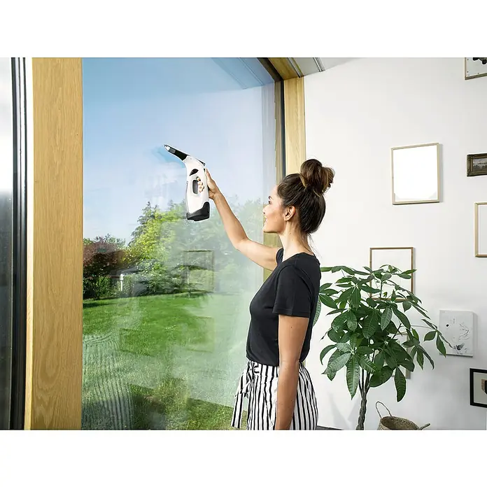 Kärcher Akku-Fenstersauger WV 2 Plus DH - 3,7 V, Behältervolumen: 0,1 l - Frau putzt Fenster mit Kärcher Fenstersauger für streifenfreie Sauberkeit, während sie die Aussicht genießt.