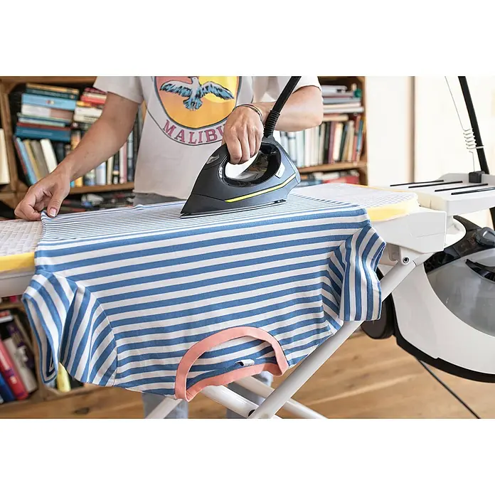 Kärcher Dampfreiniger SC 5 EasyFix Iron - 2.250 W, Aufheizzeit: 3 min, Behältervolumen: 1,5 l - Eine Person bügelt ein blau-weiß gestreiftes T-Shirt auf einem Bügelbrett. Das Bügeleisen ist schwarz mit gelben Akzenten.