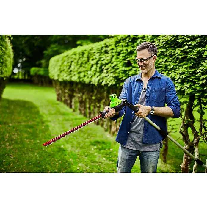 Greenworks 60V Akkusystem Teleskop-Heckenschere GD60PHT51 - 60 V, Li-Ionen, Ohne Akku, Schnittlänge: 51 cm - Ein Mann benutzt eine Heckenschere im Garten, um die Büsche zu schneiden. Die Heckenschere ist rot und grün.