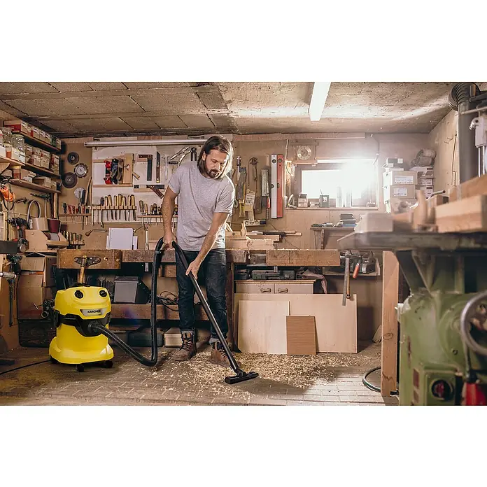 Kärcher Elektro-Nass- & Trockensauger WD 4 V-20/5/22 - 1.000 W, 20 l - Ein Mann reinigt seine Werkstatt mit einem gelben Kärcher Mehrzwecksauger, um Staub und Späne zu entfernen.