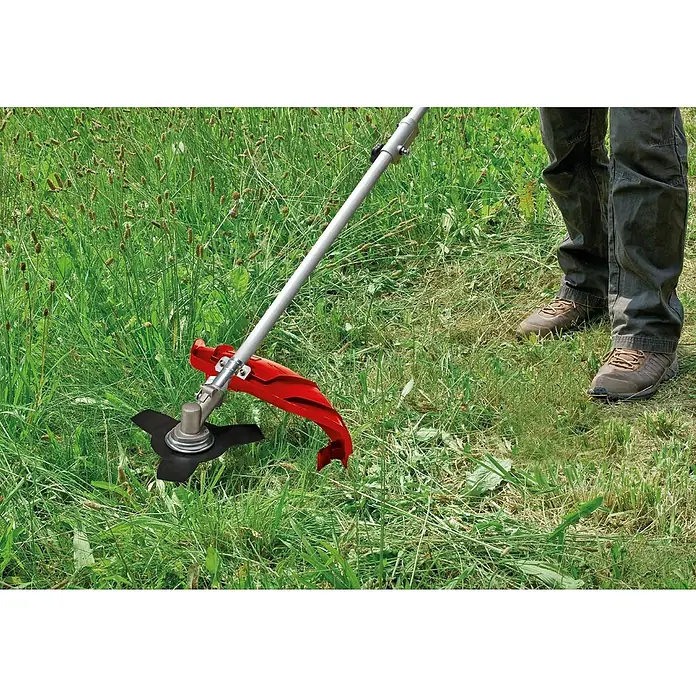 Einhell Desbrozadora de gasolina GC-BC 36-4S - 1 kW, 37,7 cm³, Ancho de corte hilo: 42 cm, Ancho de corte cuchilla: 25 cm - Desbrozadora en acción: Primer plano de la desbrozadora con protección roja y cuchilla de corte negra cortando hierba, operada por una persona.
