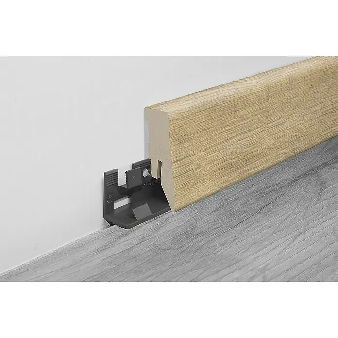 LOGOCLIC Sockelleiste Fan oak - 260 x 18 x 50 mm, MDF - Nahaufnahme einer Sockelleiste in Holzoptik, befestigt mit einem grauen Clip an einer weißen Wand über einem grauen Boden.