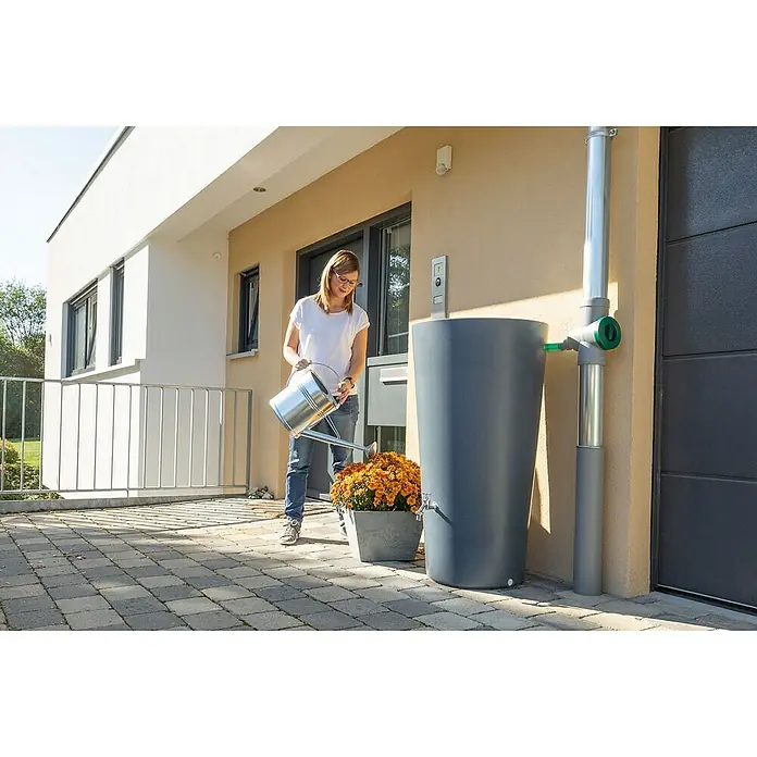 Arves Regenspeicher Rainbowl - 210 l, Betongrau - Regenspeicher mit einer Frau, die Blumen gießt. Der Regenspeicher ist aus grauem Kunststoff und steht vor einer Hauswand.