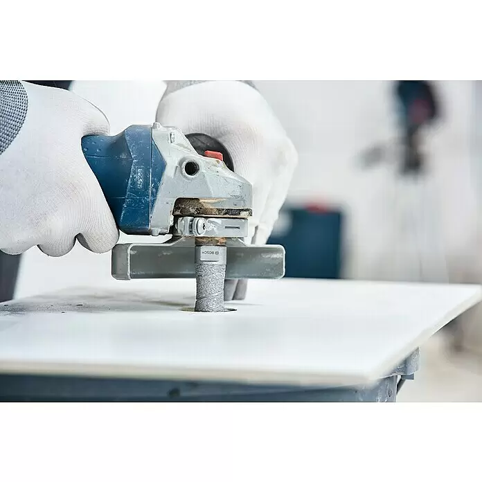 Bosch Diamant-Trockenbohrer Dry Speed - Durchmesser: 8 mm - Behandschuhte Hände bedienen einen Bosch Winkelschleifer mit zylindrischem Bohrer auf einer weißen Fliese.