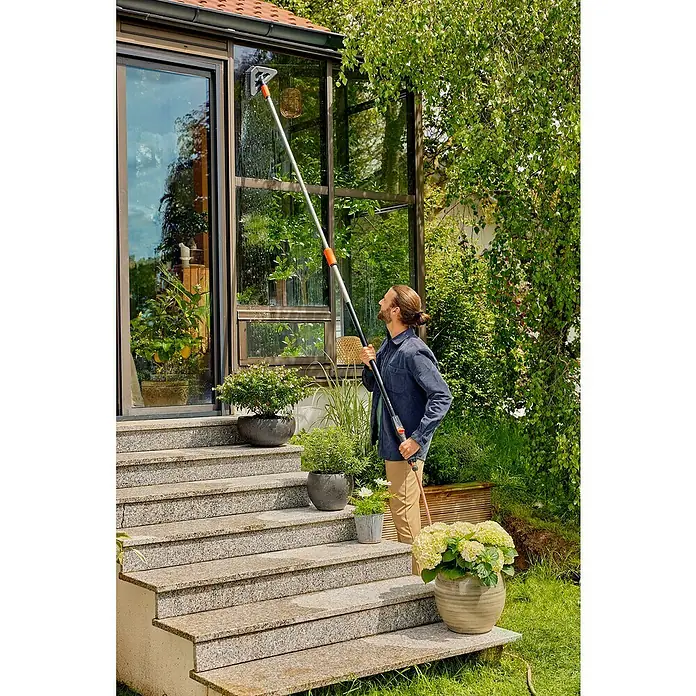 Gardena Gelenk-Schrubber Cleansystem - Abwinkelbares Gelenk - Mann reinigt mit einer Teleskopstange und Fensterwischer die Fenster des Wintergartens.