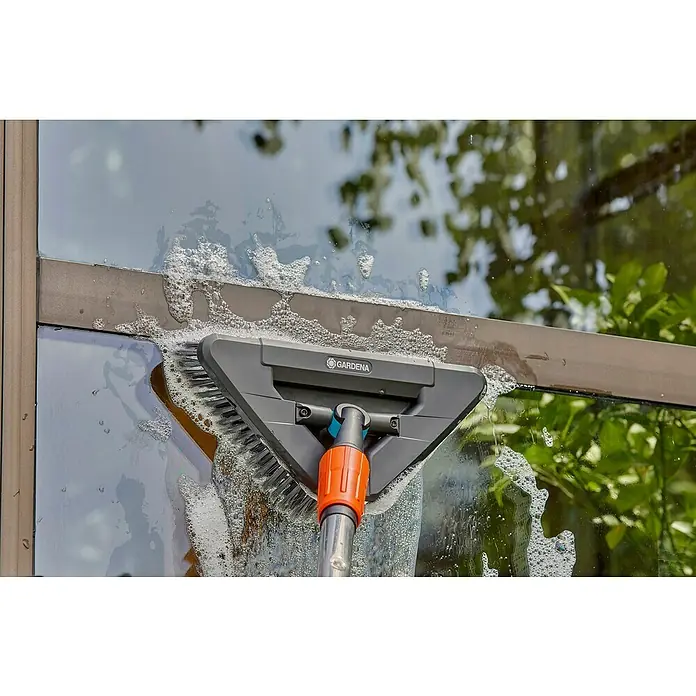 Gardena Gelenk-Schrubber Cleansystem - Abwinkelbares Gelenk - Gardena Fensterputzbürste reinigt Fenster mit Seifenwasser, während das Licht Bäume und Himmel reflektiert.