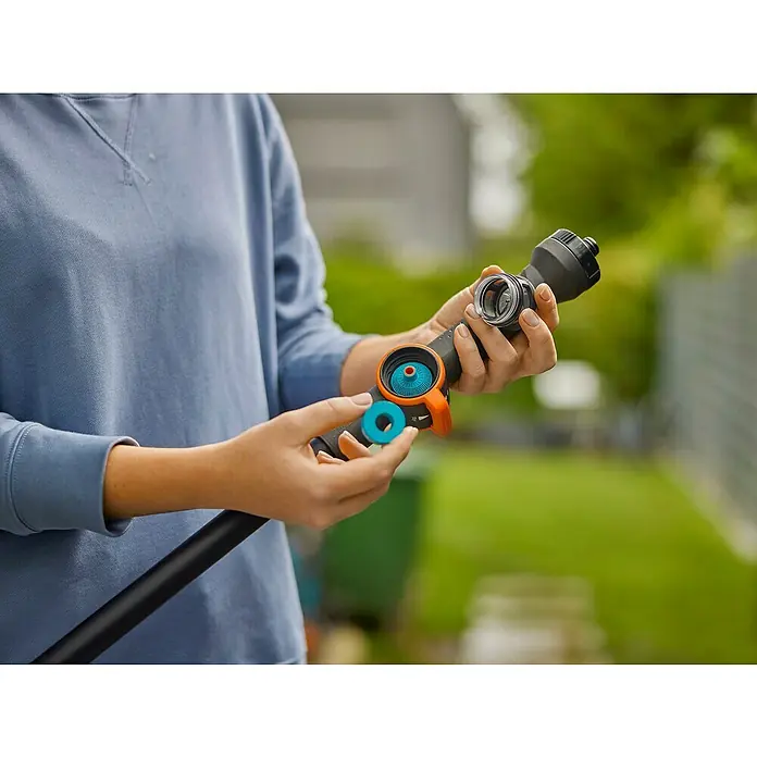 Gardena Cleansystem Wasserstiel Cleansystem - Länge Stiel: 150 cm, Aluminium - Nahaufnahme einer Person, die eine GARDENA-Gartenspritze mit blau-orangenen Akzenten hält, während sie diese an einen Gartenschlauch anschließt.