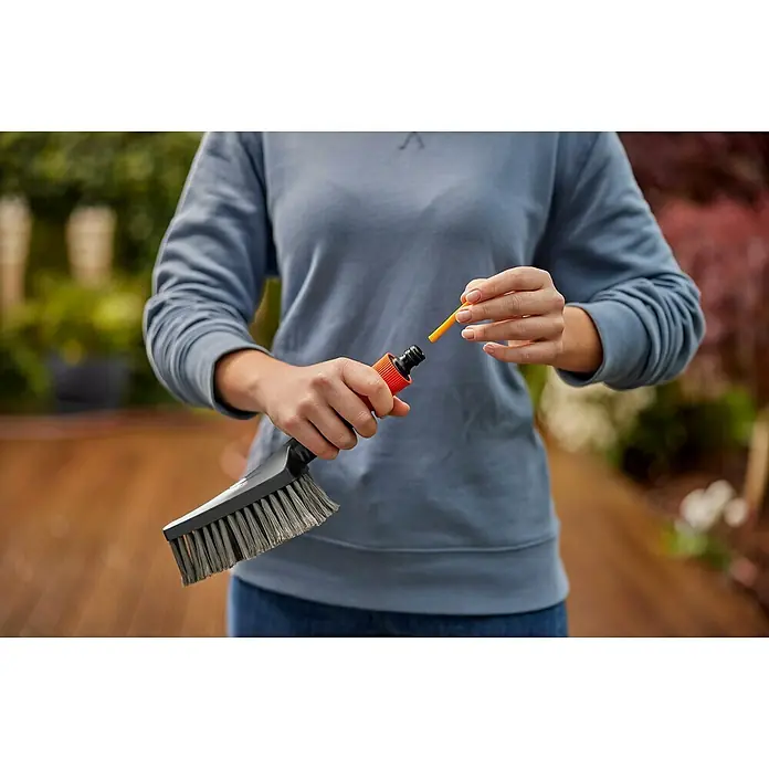 Gardena Komfort-Handbürste Cleansystem S soft - Wasserführend - Eine Person setzt eine orangefarbene Reinigungsnadel in eine Bürste mit Wasseranschluss. Ideal für die Reinigung von Gartenmöbeln und Terrassen.