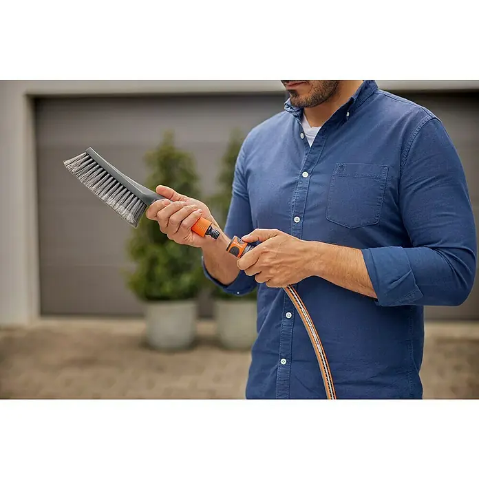 Gardena Komfort-Handbürste Cleansystem S soft - Wasserführend - Eine Person in einem blauen Hemd, die eine Gardena Waschbürste mit Wasseranschluss in den Händen hält, um Oberflächen zu reinigen.