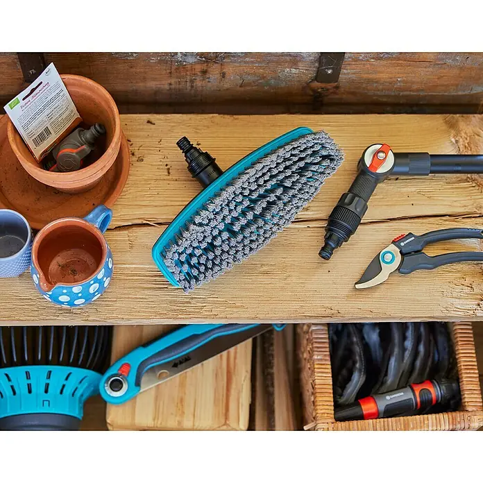 Gardena Cleansystem Waschbürste Cleansystem - Wasserführend - Nahaufnahme von Gartengeräten, darunter eine Bürste, eine Gartenschere und Töpfe, die auf einem Holzregal angeordnet sind.