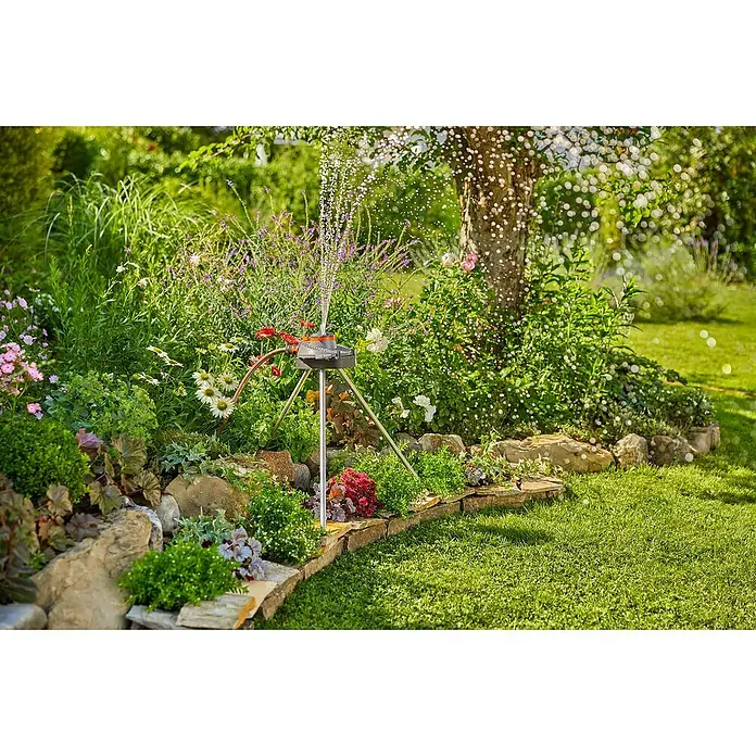 Gardena Stativ - Kunststoff - Bewässerung im Garten mit einem GARDENA Regner auf einem Rasen mit Blumen und Steinen. Das Gerät ist ideal für die Gartenbewässerung.