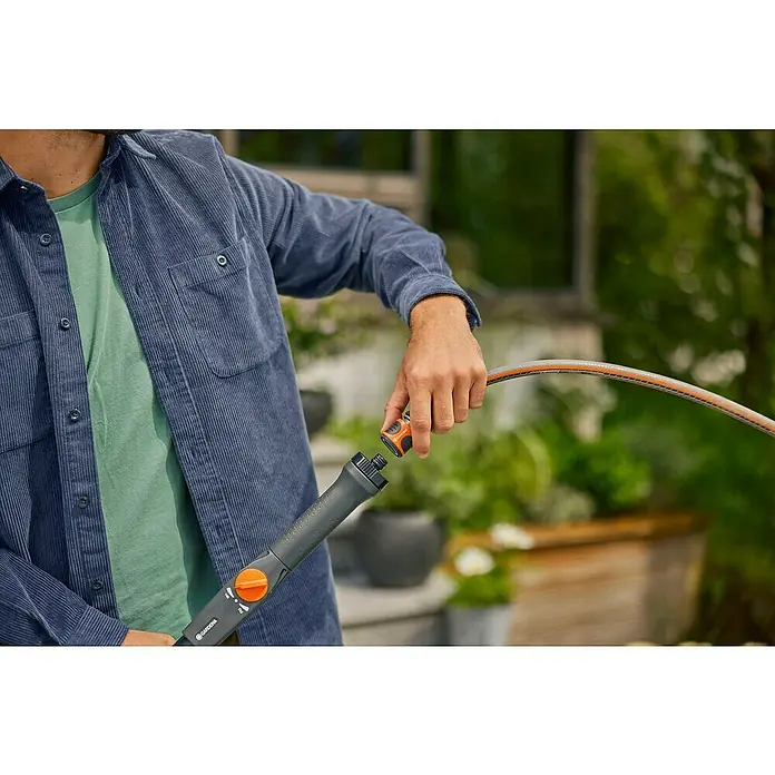 Gardena Cleansystem Teleskop-Wasserstiel Cleansystem - 155 cm - 260 cm, Aluminium - Ein Mann schließt einen orangefarbenen Gardena-Schlauchverbinder an ein graues Sprühgerät an, ideal für die Gartenbewässerung.