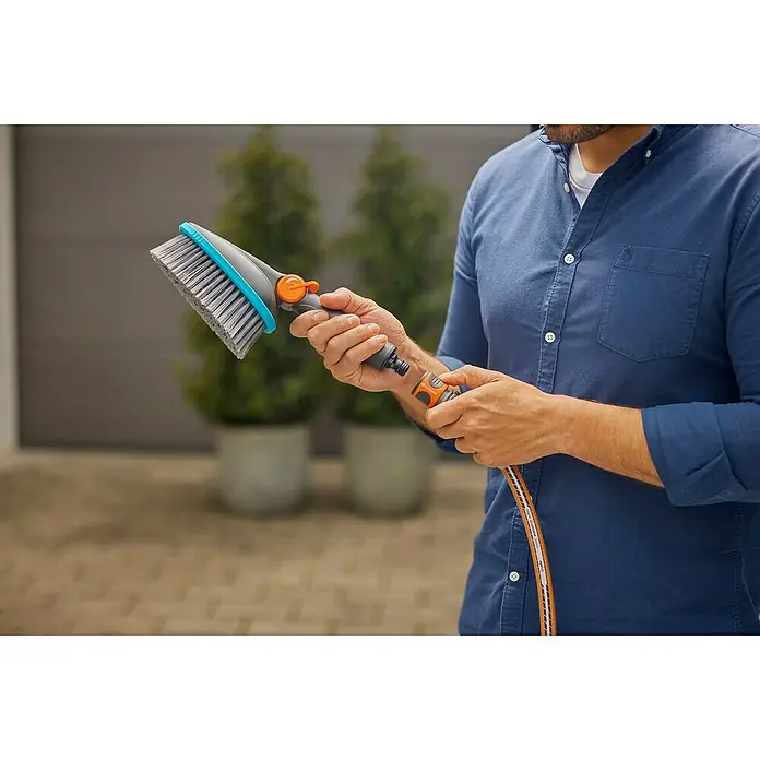 Gardena Cleansystem Komfort-Handbürste Cleansystem M soft - Wasserführend - Nahaufnahme einer Person, die eine GARDENA Waschbürste mit Wasseranschluss in der Hand hält, ideal für Reinigungsarbeiten im Freien.