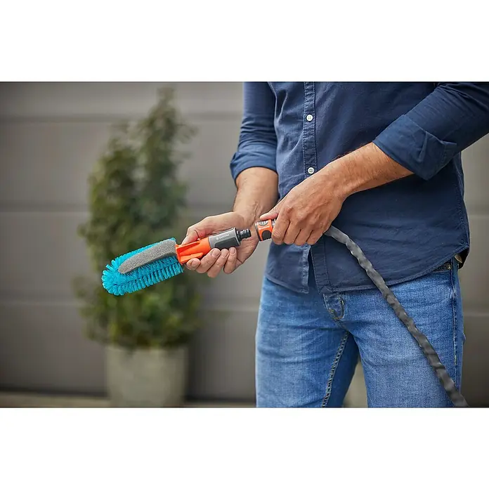 Gardena Reinigungsbürste Cleansystem - Wasserführend - Ein Mann hält eine GARDENA Waschbürste mit Rotationswasserdüse, ideal für die Autopflege, mit blauem Bürstenkopf und grauem Schwamm.